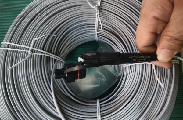 Emphasize side view of coil and connector for installation context. Side view of gray coiled fiber optic cable with black connector protruding.