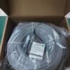 Illustrate packaged cable in open box for unboxing or sales demo. Open cardboard box containing plastic-wrapped gray fiber optic cable coil with label.
